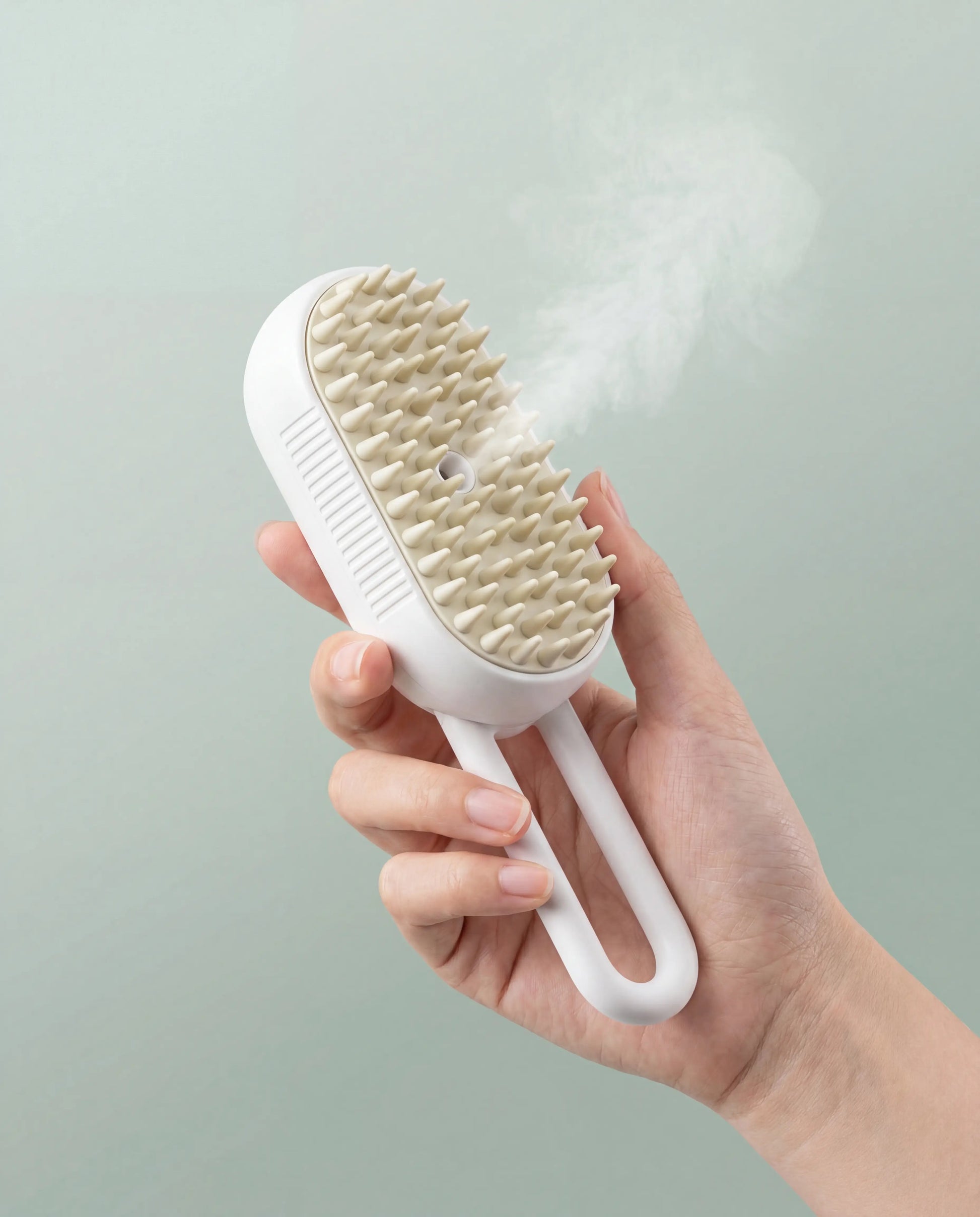 Fine mist rising from the white Sleekpaw Mist & Massage Brush held in hand